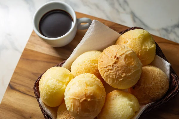 Bir fincan kahve ve peynirli çörek. Peynir ekmeği dolu küçük bir hasır sepet ve tahtadan bir yüzey üzerinde kahve olan beyaz bir fincan. Kahvaltı..