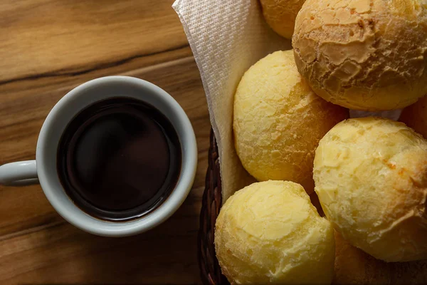 Bir fincan kahve ve peynirli çörek. Peynir ekmeği dolu küçük bir hasır sepet ve tahtadan bir yüzey üzerinde kahve olan beyaz bir fincan. Kahvaltı..