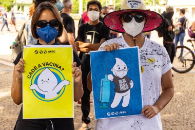 Protestoda iki protestocu bir tabela tutuyor. Protesto; Brezilya Cumhurbaşkanı Bolsonaro 'ya karşı düzenlenen bir protesto sırasında çekilen fotoğraf ve nüfusu bağışık hale getirmek için aşı satın almada çeviklik istenmesi. 