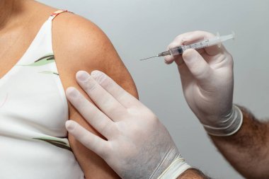 Doktorun ya da hemşirenin elleri hastanın koluna iğne yapıyor. COVID-19 'a karşı aşı.