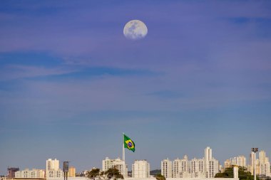 Goiania şehri rüzgarda dalgalanan bir Brezilya bayrağı ve gökteki ay ile.