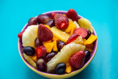 Sarı bir kasede mavi arkaplanlı meyve salatası..