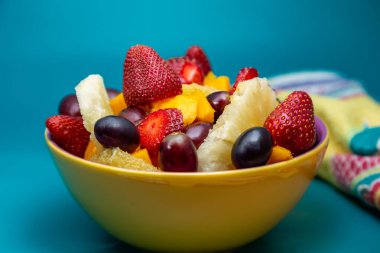 Sarı bir kasede mavi arkaplanlı meyve salatası..