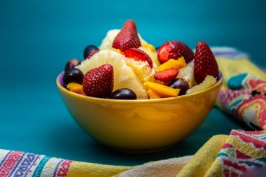 Sarı bir kasede mavi arkaplanlı meyve salatası..