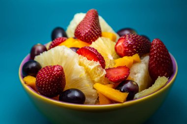 Sarı bir kasede mavi arkaplanlı meyve salatası..