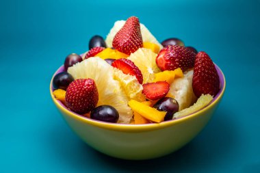 Sarı bir kasede mavi arkaplanlı meyve salatası..