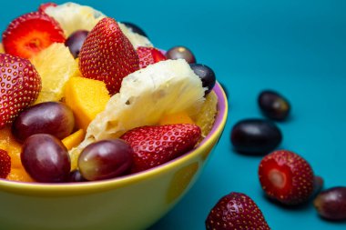 Sarı bir kasede mavi arkaplanlı meyve salatası..