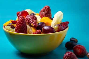 Sarı bir kasede mavi arkaplanlı meyve salatası..