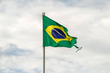 Parçalanmış, yıpranmış Brezilya bayrağı bulutlu bir günde rüzgarda dalgalanıyor..
