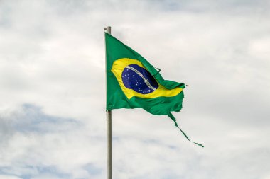 Parçalanmış, yıpranmış Brezilya bayrağı bulutlu bir günde rüzgarda dalgalanıyor..