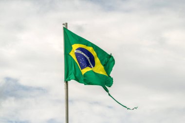 Parçalanmış, yıpranmış Brezilya bayrağı bulutlu bir günde rüzgarda dalgalanıyor..