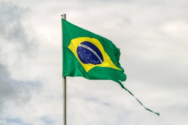 Parçalanmış, yıpranmış Brezilya bayrağı bulutlu bir günde rüzgarda dalgalanıyor..
