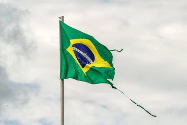 Parçalanmış, yıpranmış Brezilya bayrağı bulutlu bir günde rüzgarda dalgalanıyor..