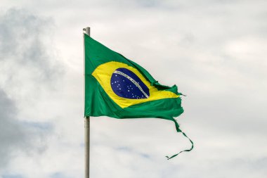 Parçalanmış, yıpranmış Brezilya bayrağı bulutlu bir günde rüzgarda dalgalanıyor..