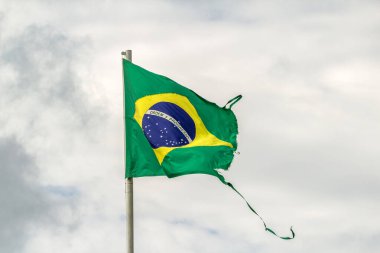 Parçalanmış, yıpranmış Brezilya bayrağı bulutlu bir günde rüzgarda dalgalanıyor..