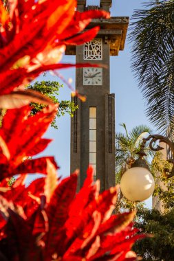 Goiania 'daki Avenida Goias' taki Art Deco saat kulesinin ayrıntıları, açık ve güneşli bir günde kırmızı yapraklı bitkiler tarafından çerçevelenmiş..