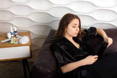 Genç kadın evde hasta, tabletlerdeki sosyal ağları okuyor.