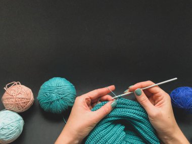 Tığ işi, turkuaz iplik ve siyah arka plan. İplik yumağı ve örgü kancası. Kendi ellerinle bir ürün yaratma kavramı. İğne işi, hobiler.