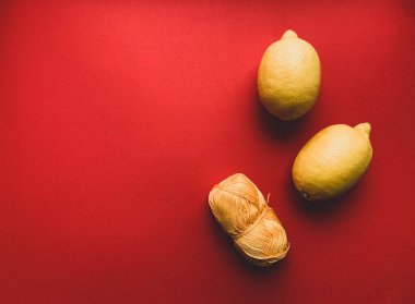 Kırmızı arka planda iki sarı limon ve bir sarı iplik. Limon. Yukarıdan bir fotoğraf. C vitamini. Sağlık tanıtımı. Sarı meyvelerin fotoğrafları. Sarı ve kırmızı renkler..