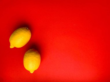 Kırmızı arka planda iki sarı limon. Limon. Yukarıdan bir fotoğraf. C vitamini. Sağlık tanıtımı. Sarı meyvelerin fotoğrafları.