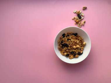 Beyaz kase, yumuşak pembe arka planda ev yapımı granola. Üstten manzaralı bir fotoğraf. Düzgün beslenme, sağlıklı kahvaltı..