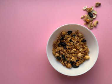 Beyaz kase, yumuşak pembe arka planda ev yapımı granola. Üstten manzaralı bir fotoğraf. Düzgün beslenme, sağlıklı kahvaltı..