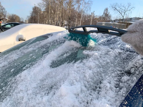 Cleaning the car from snow with a brush. In the photo, the girl cleans the car from the snow. Snow removal, keeping the car clean. Winter weather, snowfall