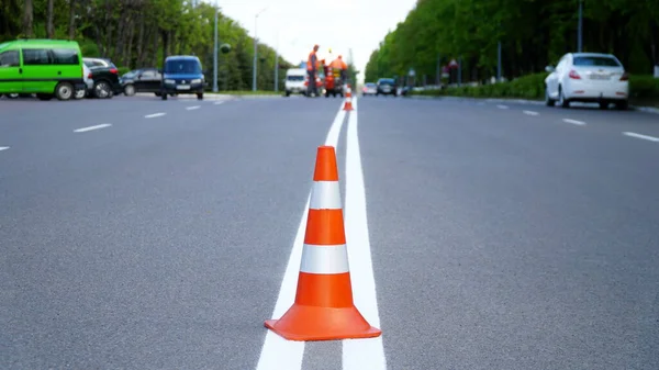 Macro shot of road traffic cones with orange and white stripes standing on street on gray asphalt during road construction works. Just painted white street lines on pedestrian crossing