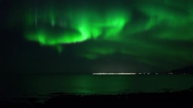 Okyanusa yansıyan gerçek zamanlı Aurora Borealis uzak İzlanda kasabası üzerinde
