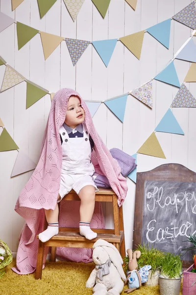 Beautiful little baby boy sitting on a chair with a knitted blanket Easter basket with colored eggs hay, Easter Bunny, a holy religious holiday, a happy guy cute child funny kid — Stok fotoğraf