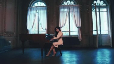 Güzel kadın giyinmiş şık zarif beyaz elbiseli, pahalı bir mücevher, bir müzik aleti, anahtarları parmak melodik büyük pencereli balo piyano konseri