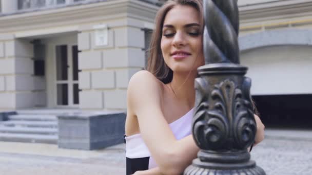 Young elegant woman came out on a date flirting turned gently looks at the camera wearing a fashion dress with open shoulder evening make-up hair swaying in the warm summer breeze — Stock Video