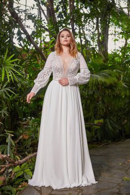 Güzel bir kadın ve manken bir gelin. Parlak sarı saç, uzun ipek beyaz elbise, dantelli düğün töreni. Çiçekli bahçe partisi aksesuarları..