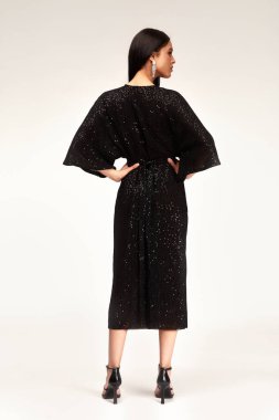 Seksi, bronz tenli, uzun esmer, açık renk makyajlı, moda partisi tarzı pullu, gece buluşması için siyah elbiseli, yüksek topuklu ayakkabılı, gösterişli, hayat tarzlı bir kadın..