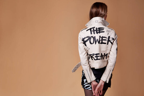Сексуальная модель брюнетка волосы носить модную одежду кожаная куртка бежевый и черная короткая юбка картина надпись слово стиль случайный дизайнер студии фон городской красивой женщины.