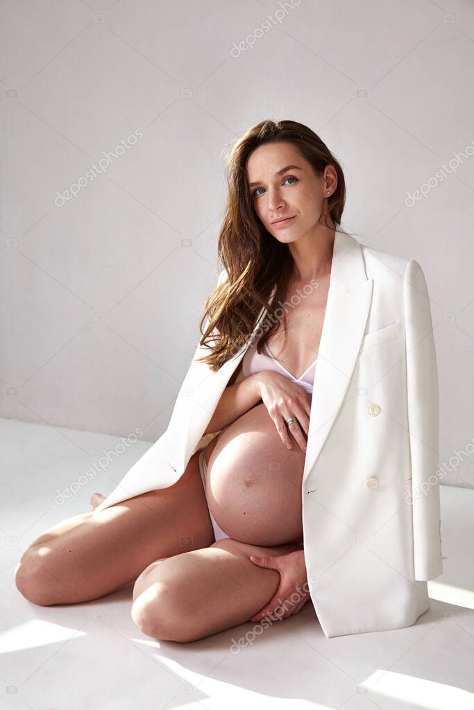 Beautiful sexy brunette woman pregnant belly lady on nine's month happy Mather white skin wear white underwear and jacket on light studio background cosmetic for body skin care fashion portraits.