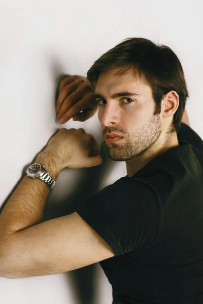 Retrato de moda de un chico guapo enojado con cabello castaño y ojos brillantes en una camiseta negra y un reloj de plata en su mano izquierda malvado mirando fijamente al marco —  Fotos de Stock