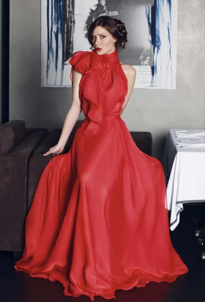 Beautiful sexy woman with beautiful makeup and red lipstick in red long evening dress of silk or chiffon with a large bow — Stock Photo, Image