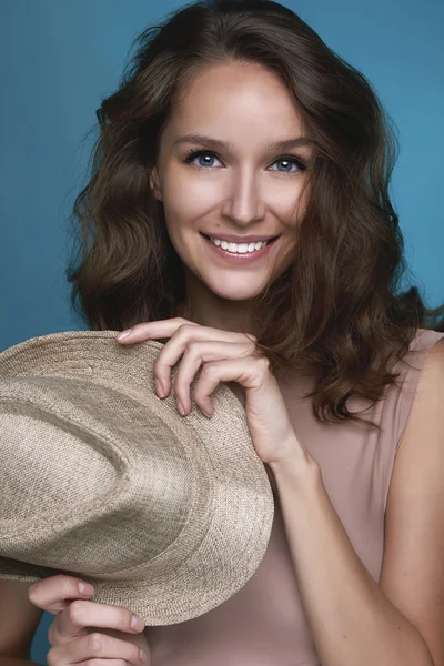 Portret van het mooie meisje met glanzende witte tanden en donker haar glimlachend op een blauwe achtergrond en houden beige stro — Stockfoto