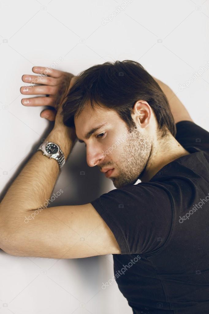 Fashion portrait of an angry handsome smartlooking guy with Brown hair and Bright eyes in a black T-shirt and silver watch on his left hand evil staring into the frame
