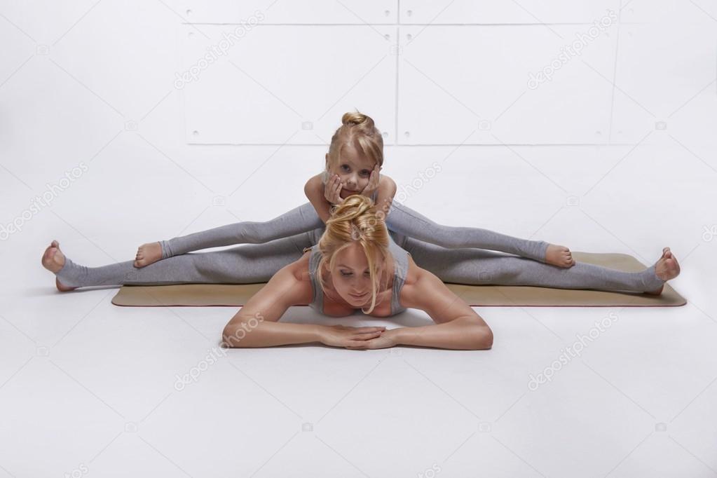 Mother daughter doing yoga exercise,fitness family sports, sports paired woman sitting on the floor stretching his legs apart in different directions pose child sits on top of the twine in  same pose
