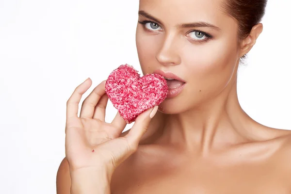 Beautiful sexy brunette woman eating cake shape of heart on a white background, healthy food, tasty, organic, romantic valentine day — Stock Photo, Image