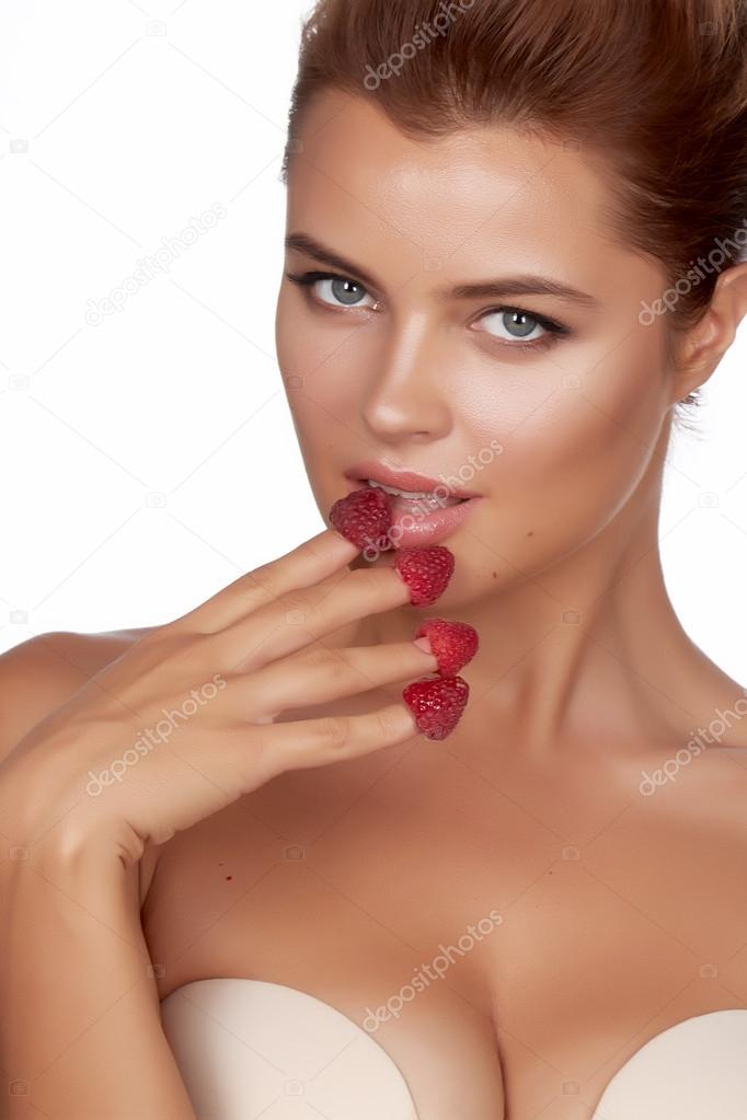 Beautiful sexy brunette woman eating raspberries on a white background, healthy food, tasty food, organic
