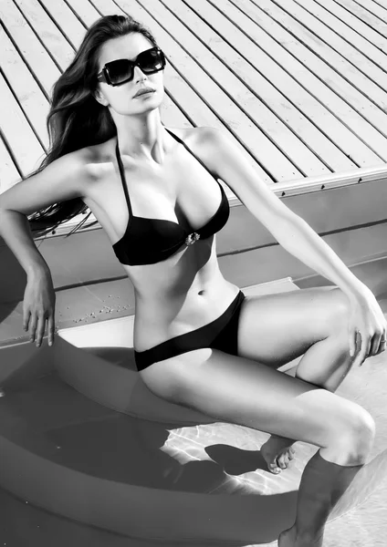Сексуальная молодая девушка с идеальной стройной фигурой с длинными мокрыми волосами и купальником в модных стильных солнцезащитных очках, сидя на ступеньках бассейна, плавает, загорает, веселится на пляжной вечеринке — стоковое фото