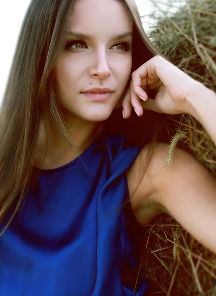 Sexy girl in a blue silk dress on a background of haystack — Stock Photo, Image