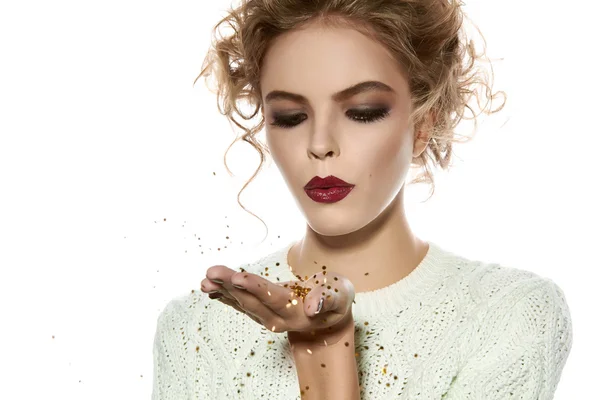 Beautiful girl with evening makeup blow gold sequins — Stock Photo, Image
