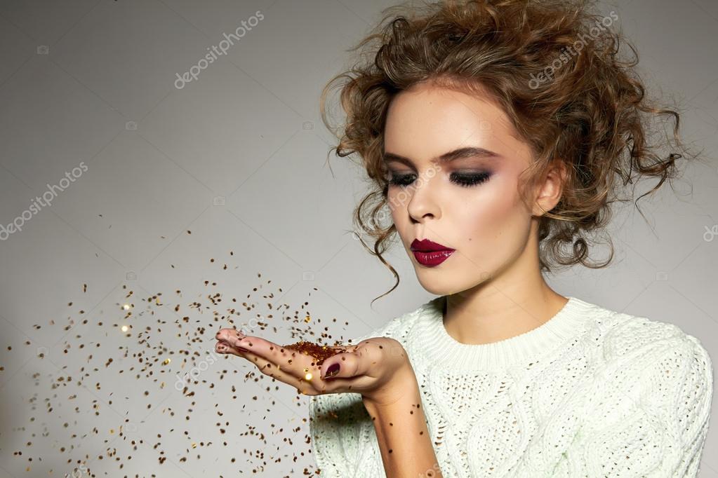 Beautiful girl with evening makeup blow gold sequins 