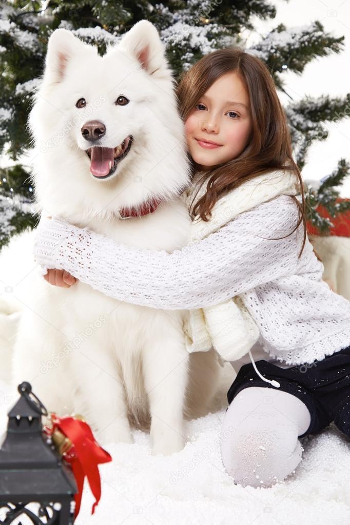 Beautiful little girl sitting in the snow at Christmas trees 