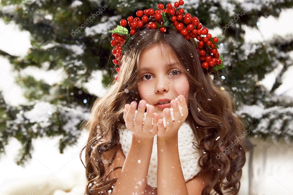 Beautiful little girl sitting in the snow at Christmas trees 