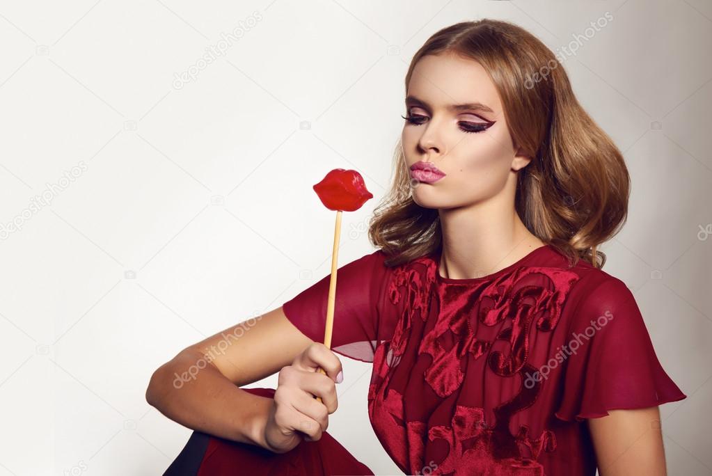 Beautiful sexy woman in silk dress with candy lips on stick